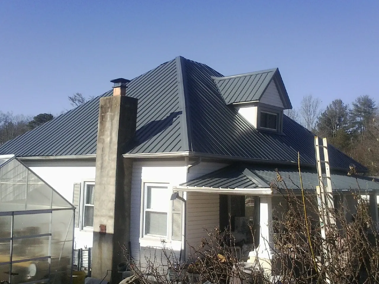 Dark blue standing seam metal roof on a white farmhouse with dormer — Slate & Tile Roof Repair by Roofing Brothers in Wolf Creek