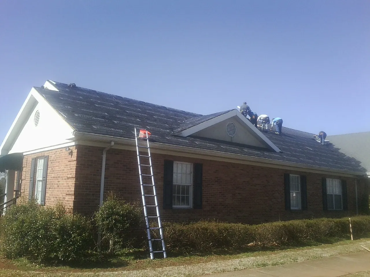 Crew tearing shingles off a brick ranch roof with a ladder set — Emergency Roof Repair work by our crew in Wolf Creek