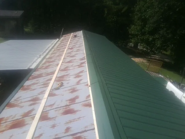Old rusted panels beside newly installed green metal roofing — Wind Damage Roof Repair by Roofing Brothers in Wolf Creek