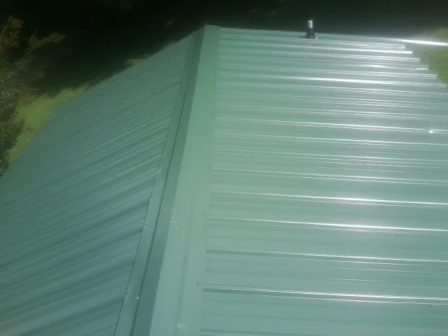 New green metal panels meeting at the ridge of a roof — Flat Roof Repair work by our crew in Wolf Creek