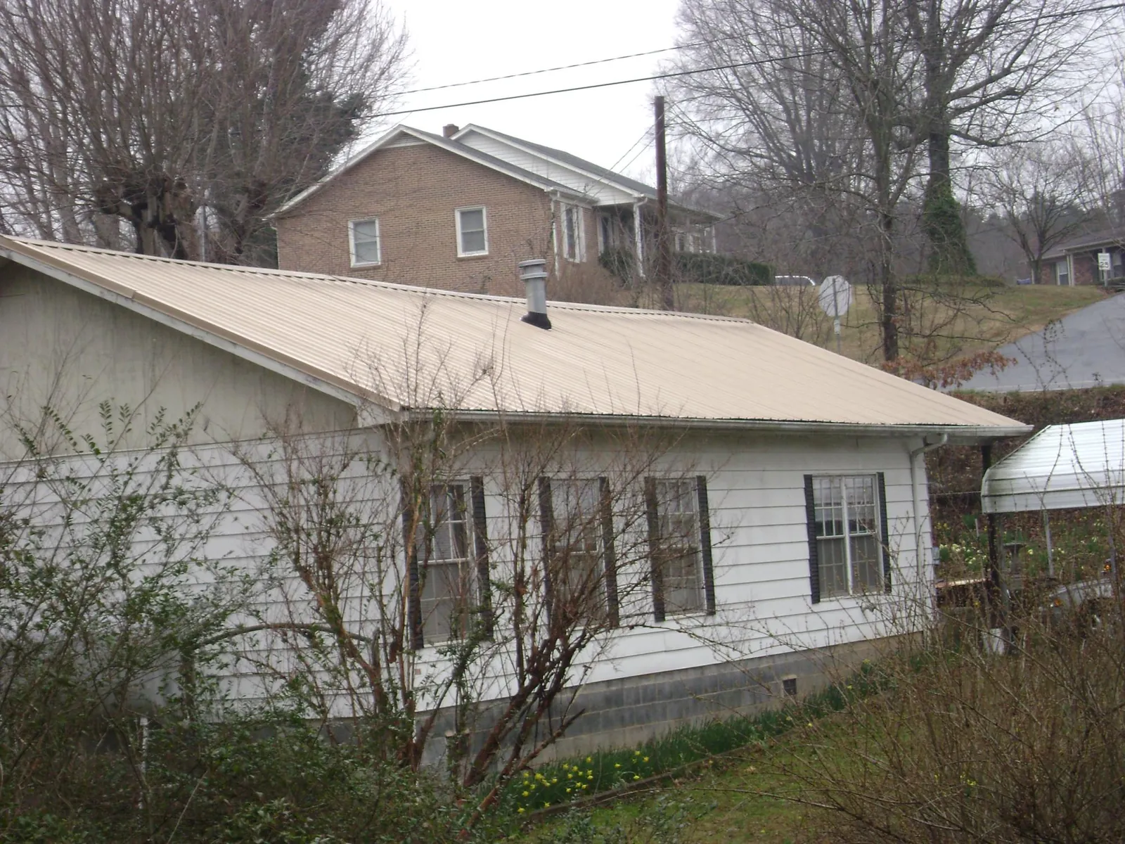 Tan metal roof on a white sided house set into a hillside — Commercial Roofing by Roofing Brothers in Wolf Creek