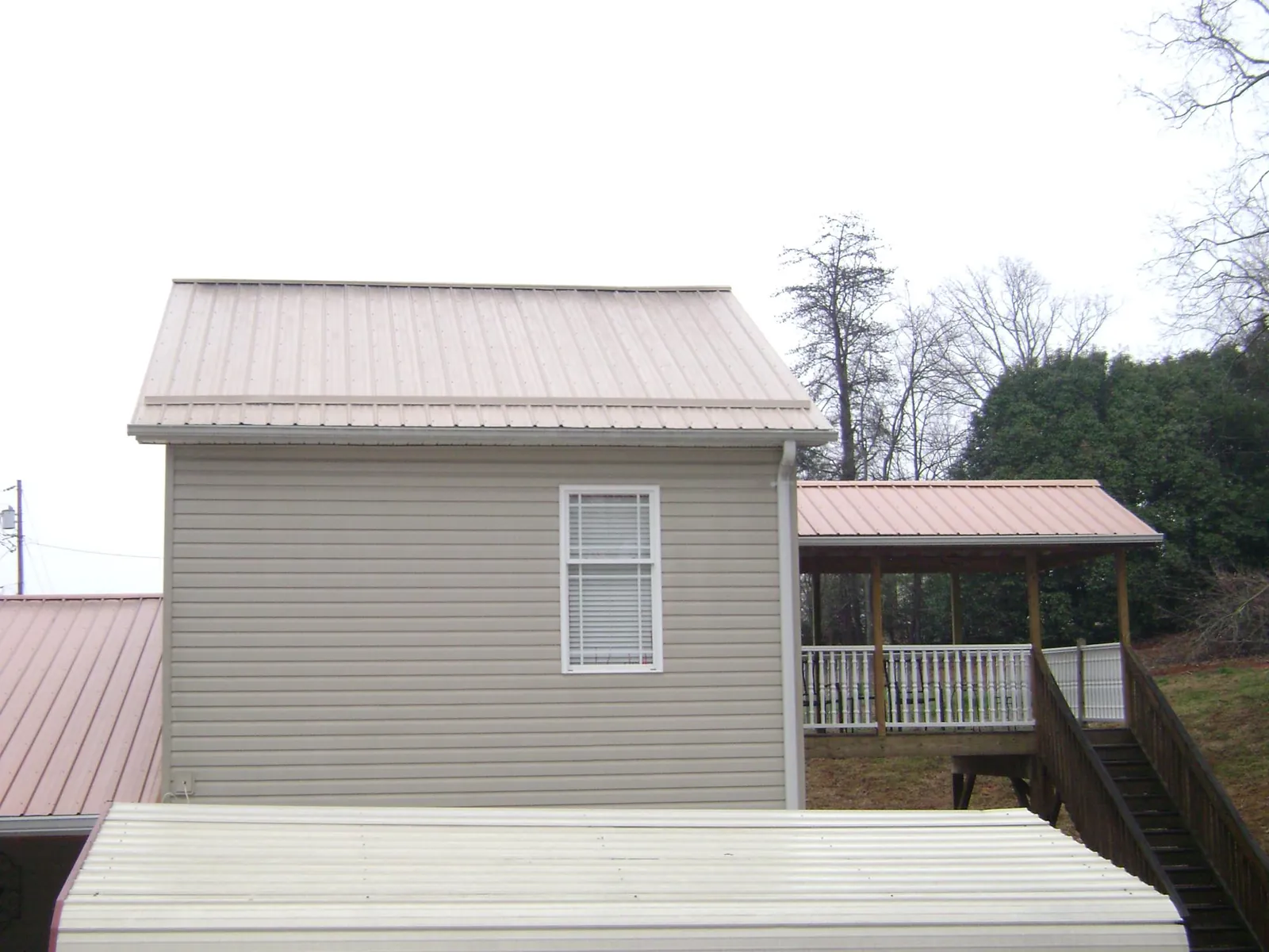 Tan metal roofs on a two story addition and attached porch, from a Roof Replacement job in Wolf Creek
